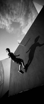 Teenage boy mid-air at a skatepark with dramatic shadows in monochrome.