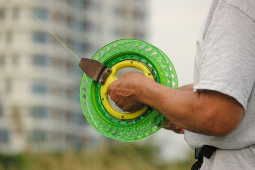 Man holding a vibrant kite reel in foreground with blurred building in background, outdoors.