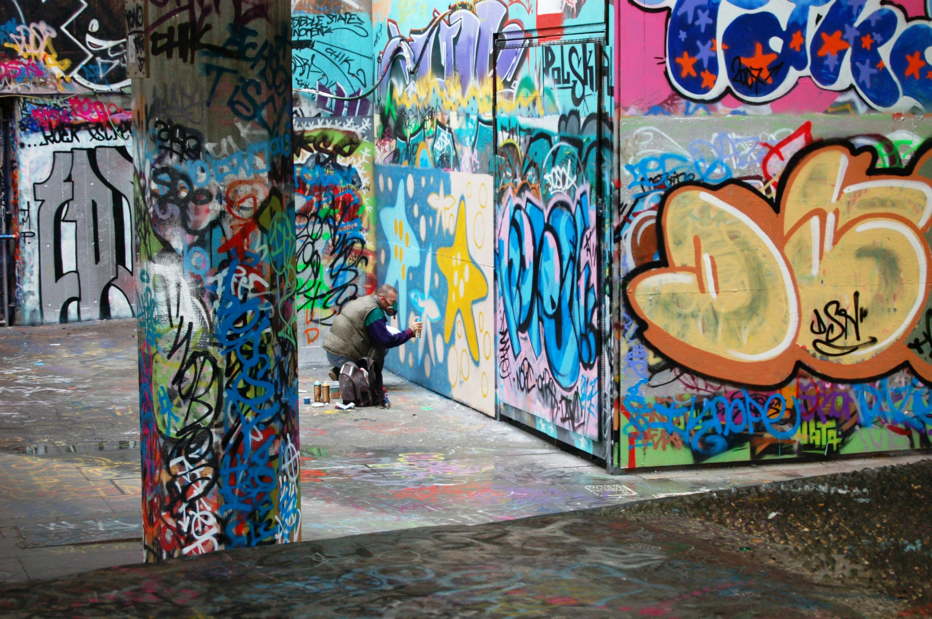 Street artist adds vibrant graffiti to urban wall in a colorful alley.