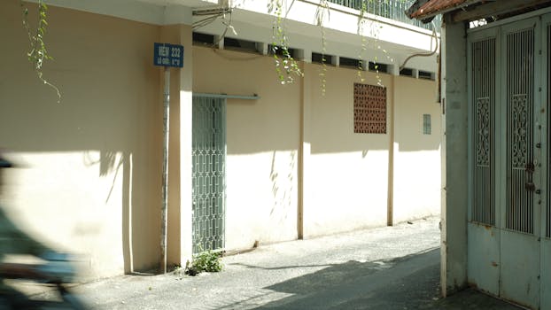 Sunlit alleyway in Vietnam with shadows and a sign reading 'Hẻm 232'.