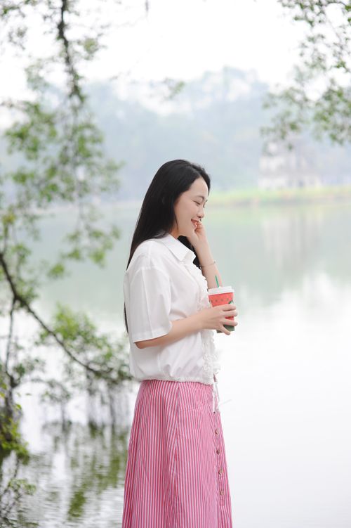 Free Young woman in summer attire holding coffee by a serene lake, embracing nature's calm. Stock Photo