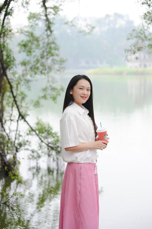 Free Smiling woman in a pink skirt holding coffee by the lake on a sunny day. Stock Photo