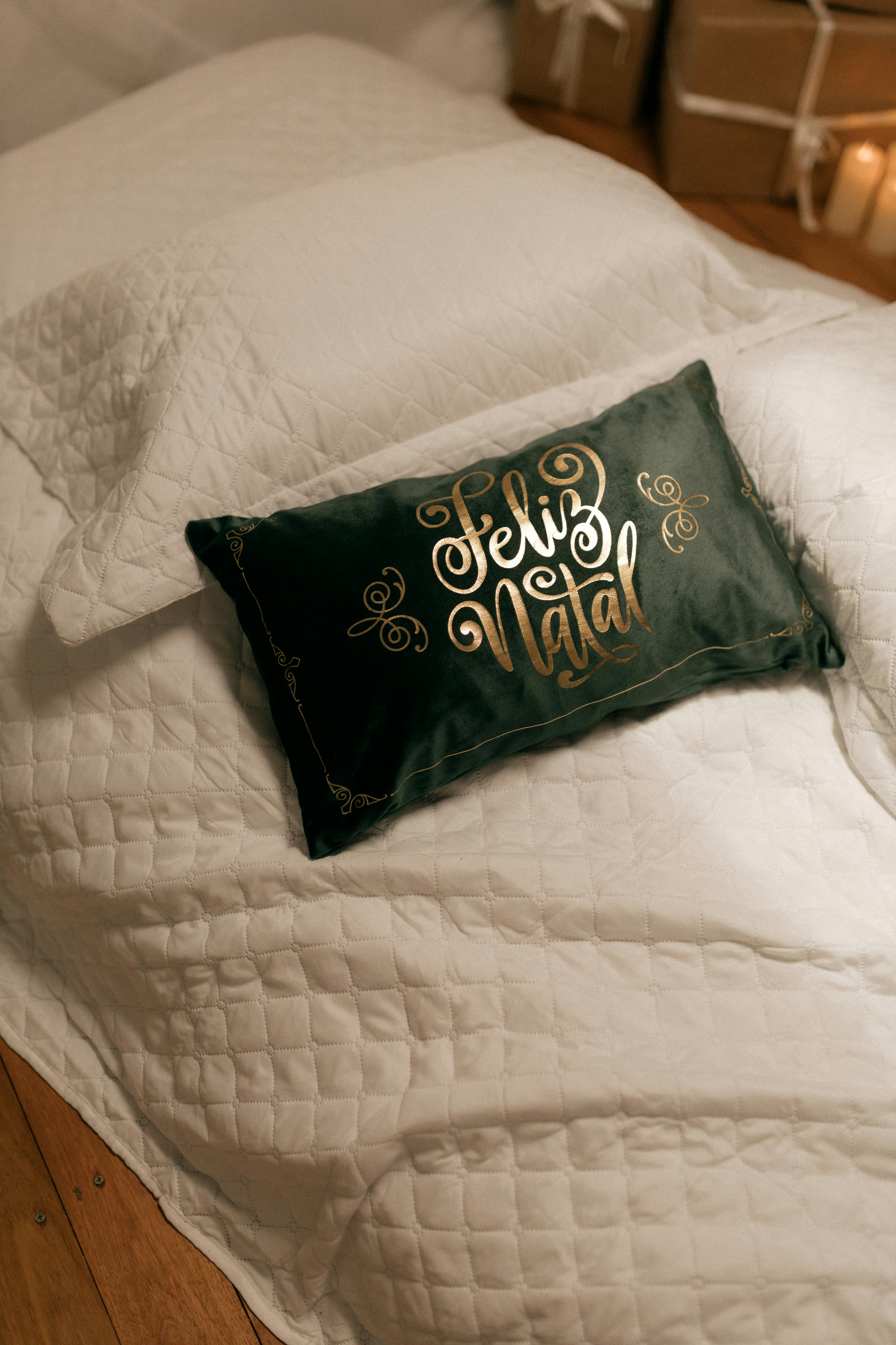 A green pillow with 'Feliz Natal' on a white quilted bedspread, creating a festive atmosphere.