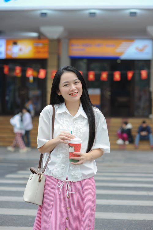 Free Woman in white blouse and pink skirt holds a drink in an urban street setting. Stock Photo