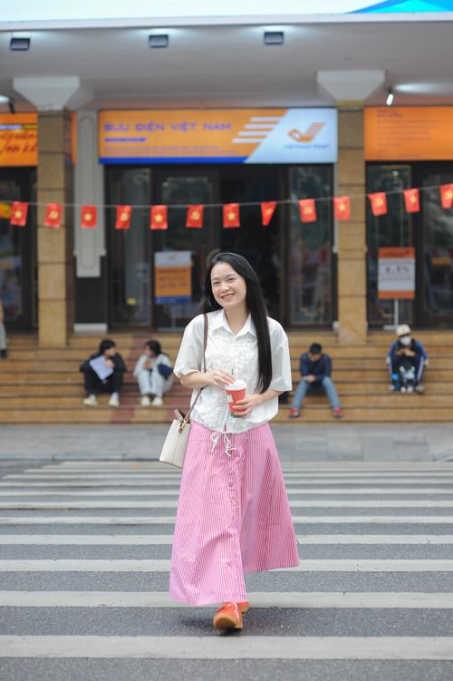 Free Smiling woman crosses street in front of post office adorned with Vietnamese flags. Stock Photo
