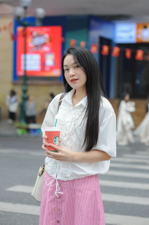Free Woman in stylish attire holding a coffee cup on a city street with vibrant signage. Stock Photo