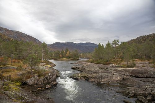Free A tranquil river flows through rocky terrain amidst lush trees in Hestad, Norway. Stock Photo