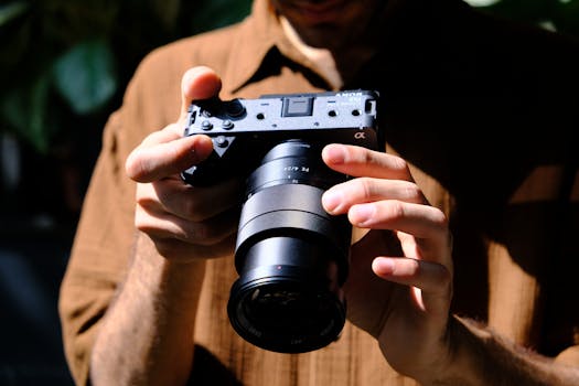 Close-up of a photographer holding a mirrorless camera outdoors in bright sunlight, creating a cinematic effect.