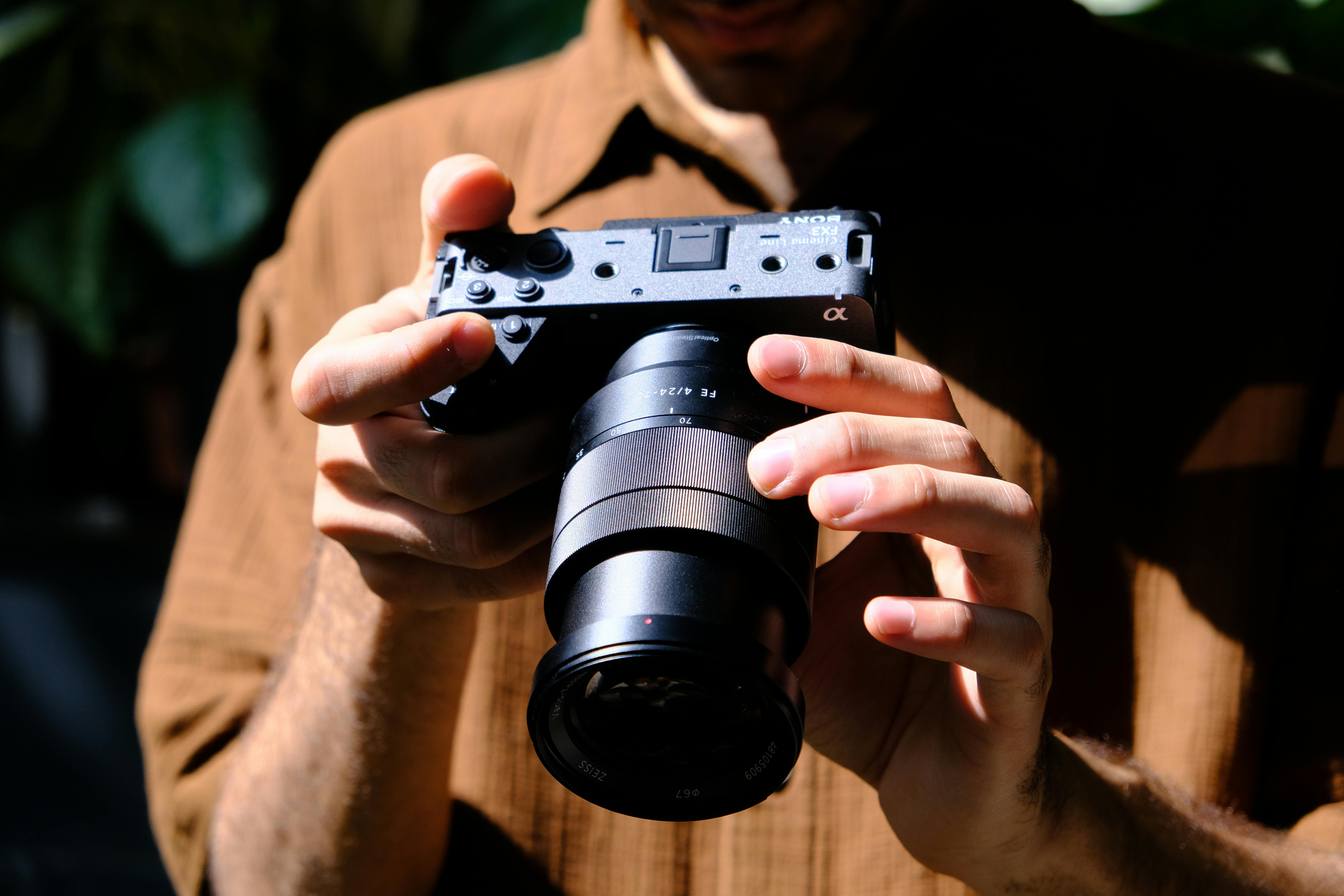 gratis Close-up van een fotograaf die buiten in het felle zonlicht een systeemcamera vasthoudt, waardoor een filmisch effect ontstaat. Stockfoto