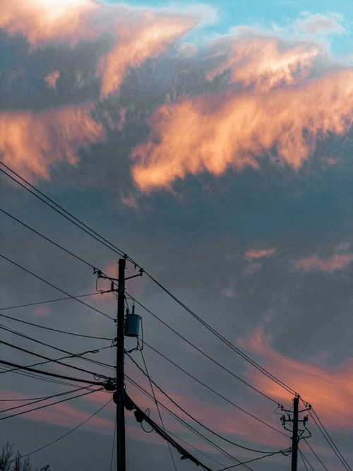 Free Vibrant clouds at sunset creating a dramatic backdrop over silhouetted power lines. Stock Photo