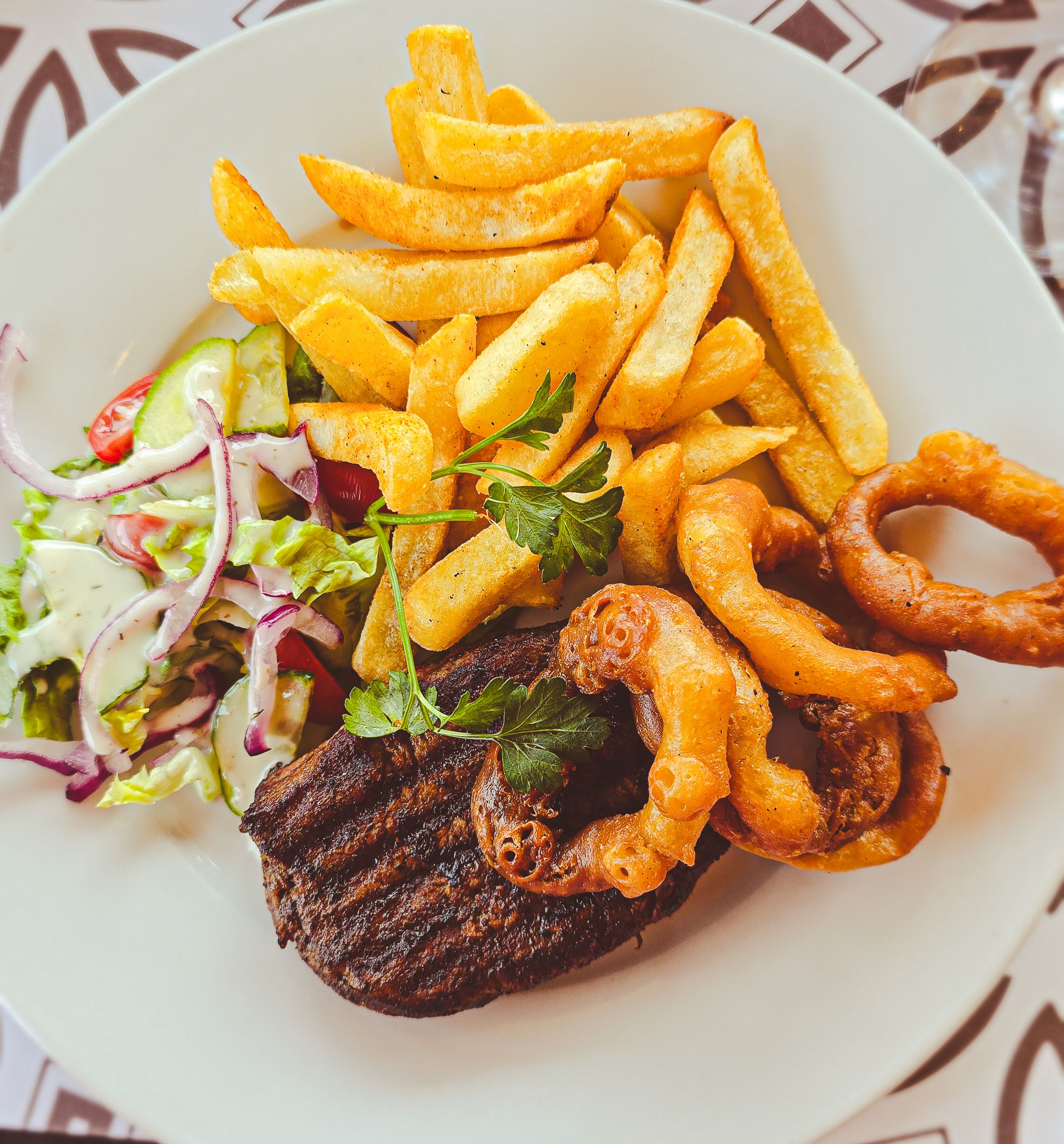 Grilled steak with crispy fries, onion rings, and fresh salad for a perfect meal.