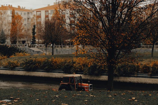 A vibrant autumn cityscape featuring a river, lush trees, and a red tractor.