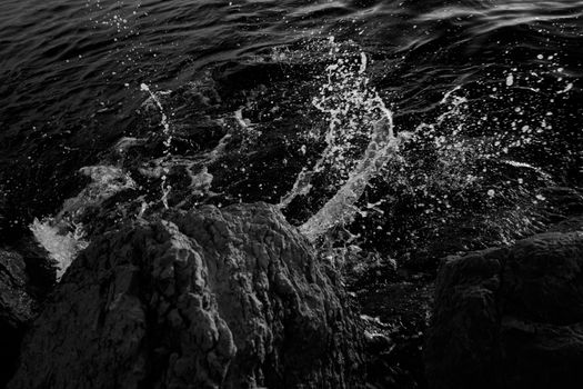 Dynamic capture of ocean waves splashing against rugged rocks in black and white.
