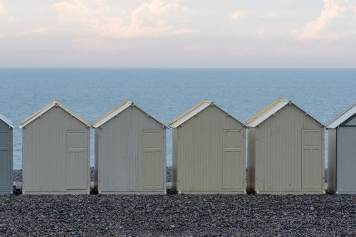 Free Coastal row of pastel beach huts on a pebble shore with ocean view. Stock Photo