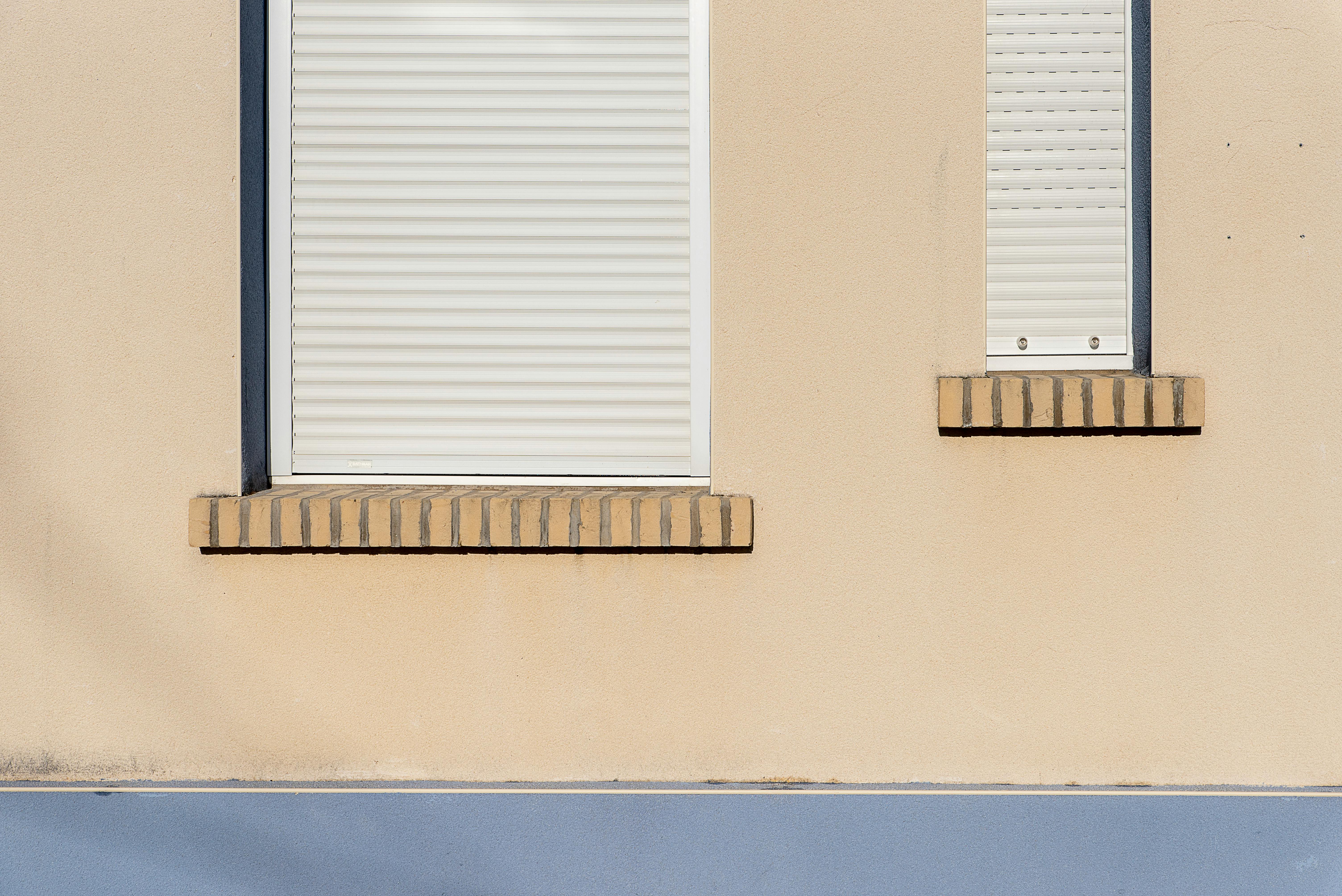 De franc Una façana d'edifici beix amb persianes enrotllables blanques tancades i un disseny arquitectònic minimalista. Foto d'estoc