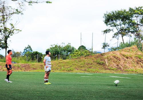 Two rugby players on a grassy field, ready for a practice session under clear skies.