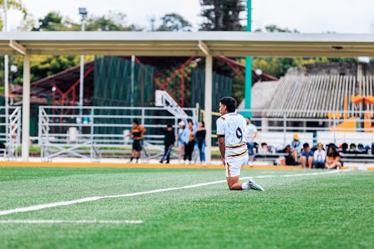 Soccer player in number 9 jersey kneeling on the field with spectators in the background.