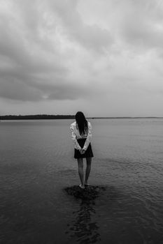 一个女人孤独地站在岸边，广阔的海洋倒映着戏剧性的天空