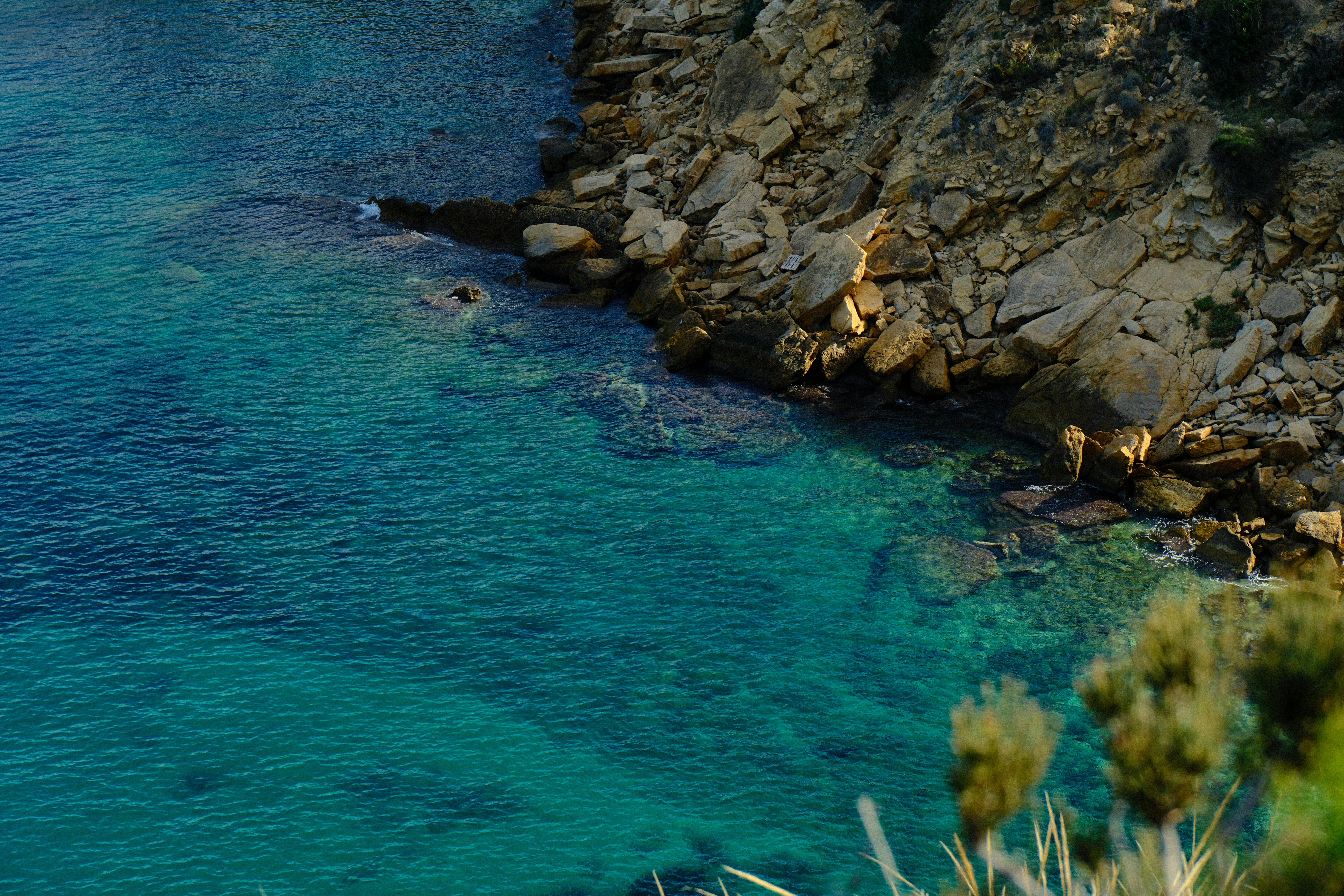 Crystal clear blue waters meeting rocky coastline in El Albir, Spain, showcasing natural beauty.