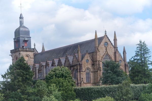 Église gothique en pierre avec clocher d'ardoise entre arbres et haies
