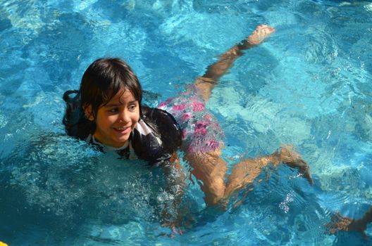 A cheerful child swimming and smiling in a sunlit pool, enjoying a summer day.