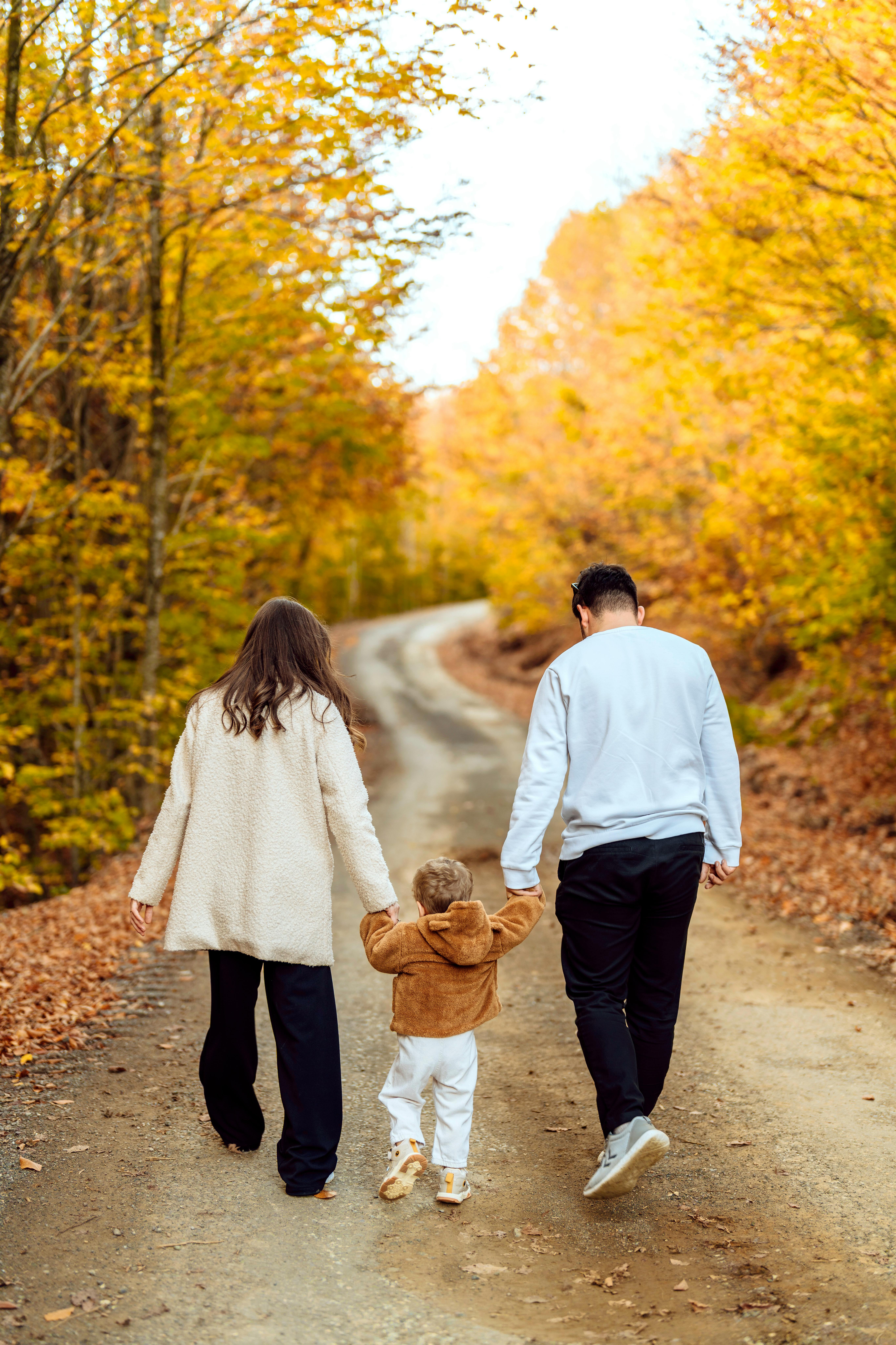 Family of three enjoying a leisurely autumn walk on a picturesque dirt road surrounded by vibrant fall foliage.