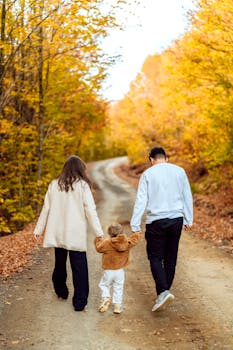 Family of three enjoying a leisurely autumn walk on a picturesque dirt road surrounded by vibrant fall foliage.