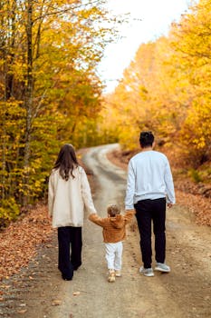 A family strolls hand in hand down a scenic autumn forest path.