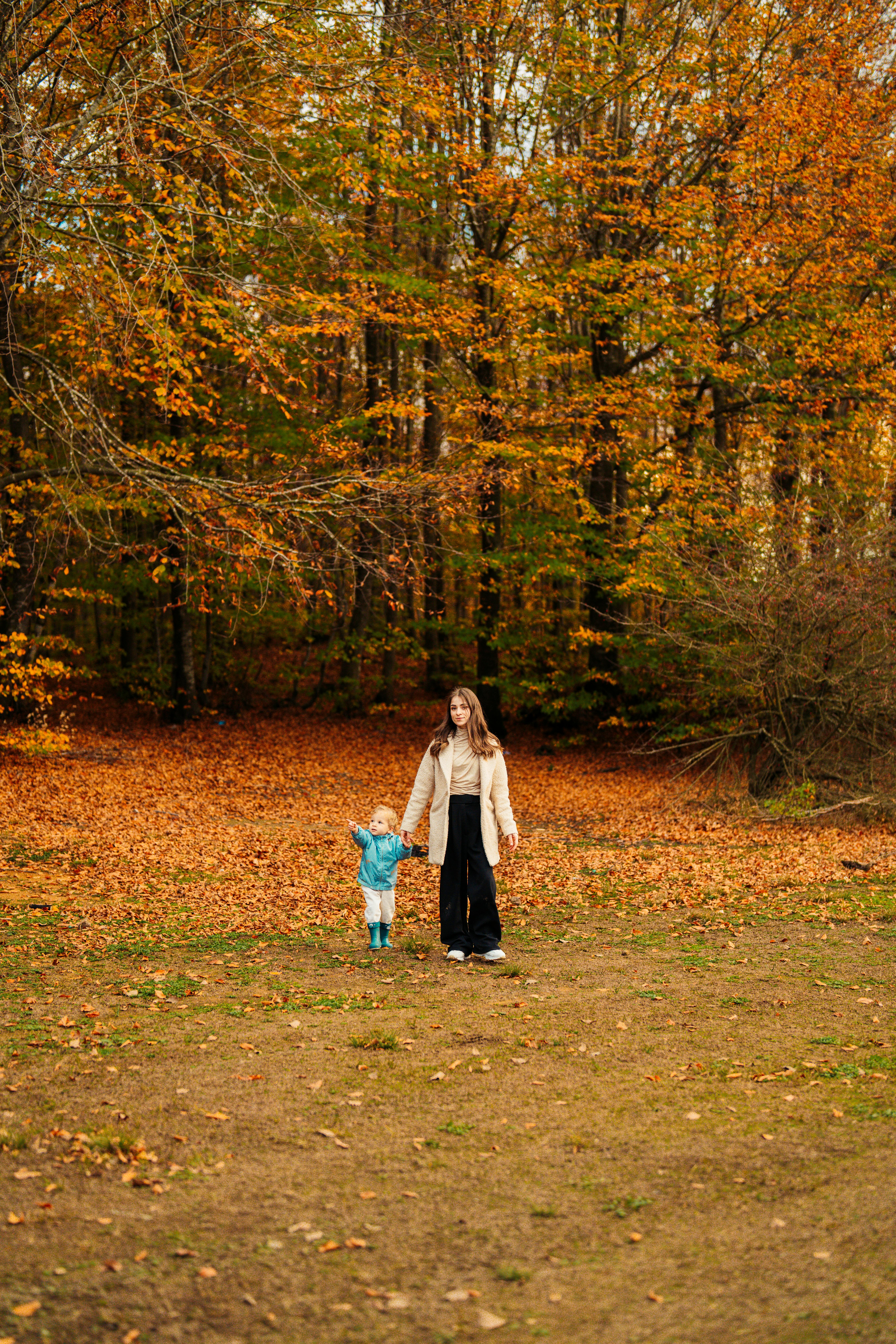 A mother and her child take a peaceful walk through a vibrant autumn forest with orange leaves.