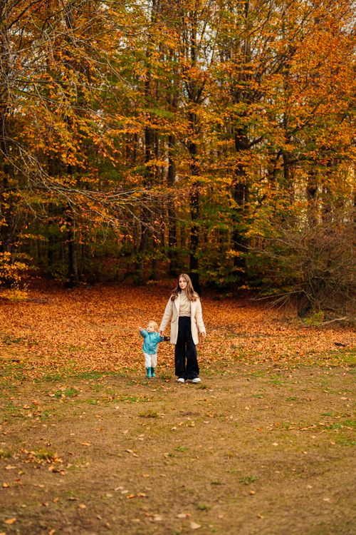 Free A mother and her child take a peaceful walk through a vibrant autumn forest with orange leaves. Stock Photo