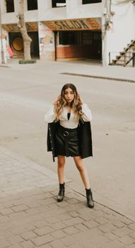 Stylish young woman poses confidently on a city street in a fashionable black outfit.