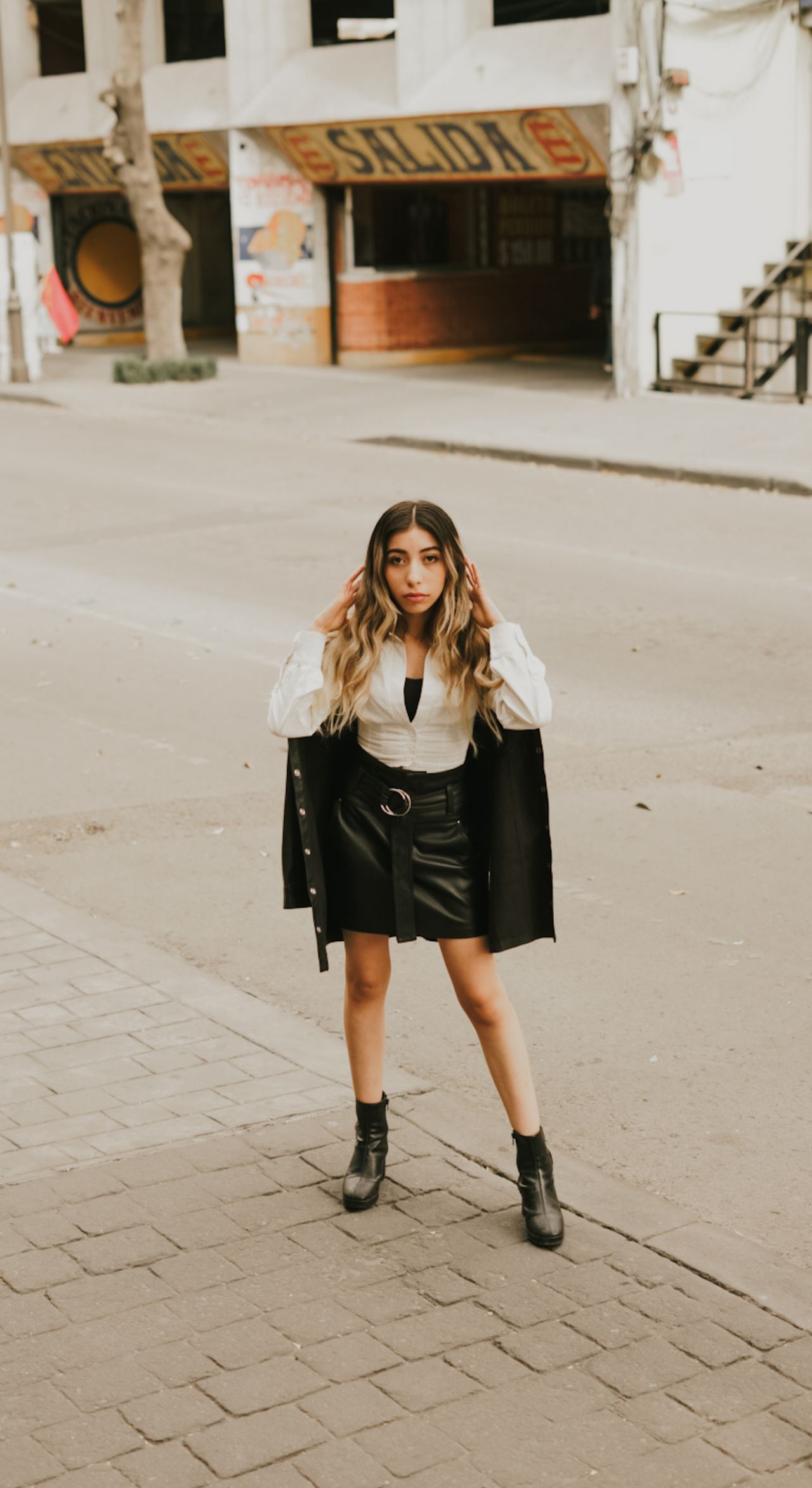 Young woman in a white top, black leather mini skirt, and ankle boots on a city street