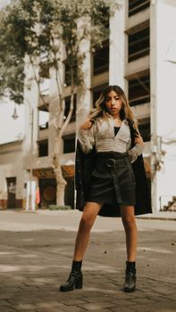 Fashionable young woman poses confidently on a sunny urban street.