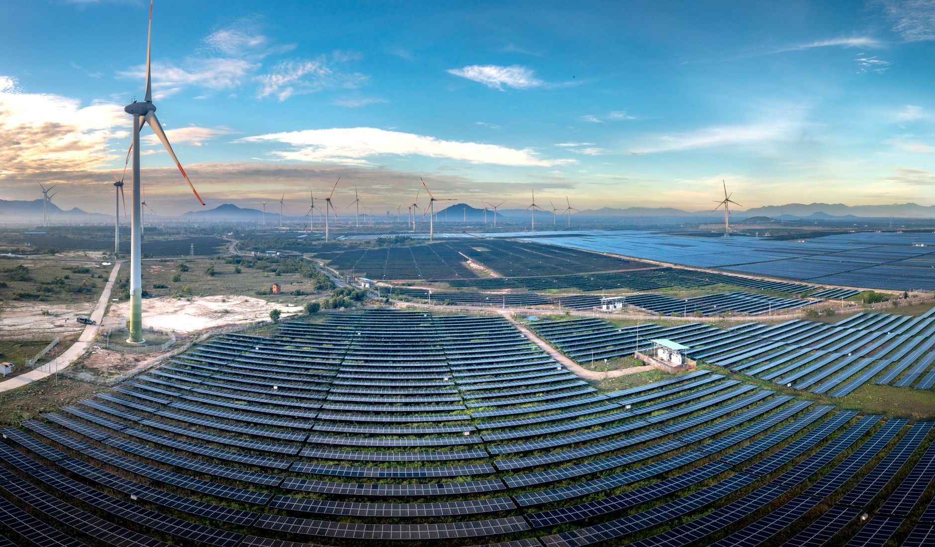 Panoramic aerial view of a renewable energy farm with solar panels and wind turbines in Vietnam at sunset.