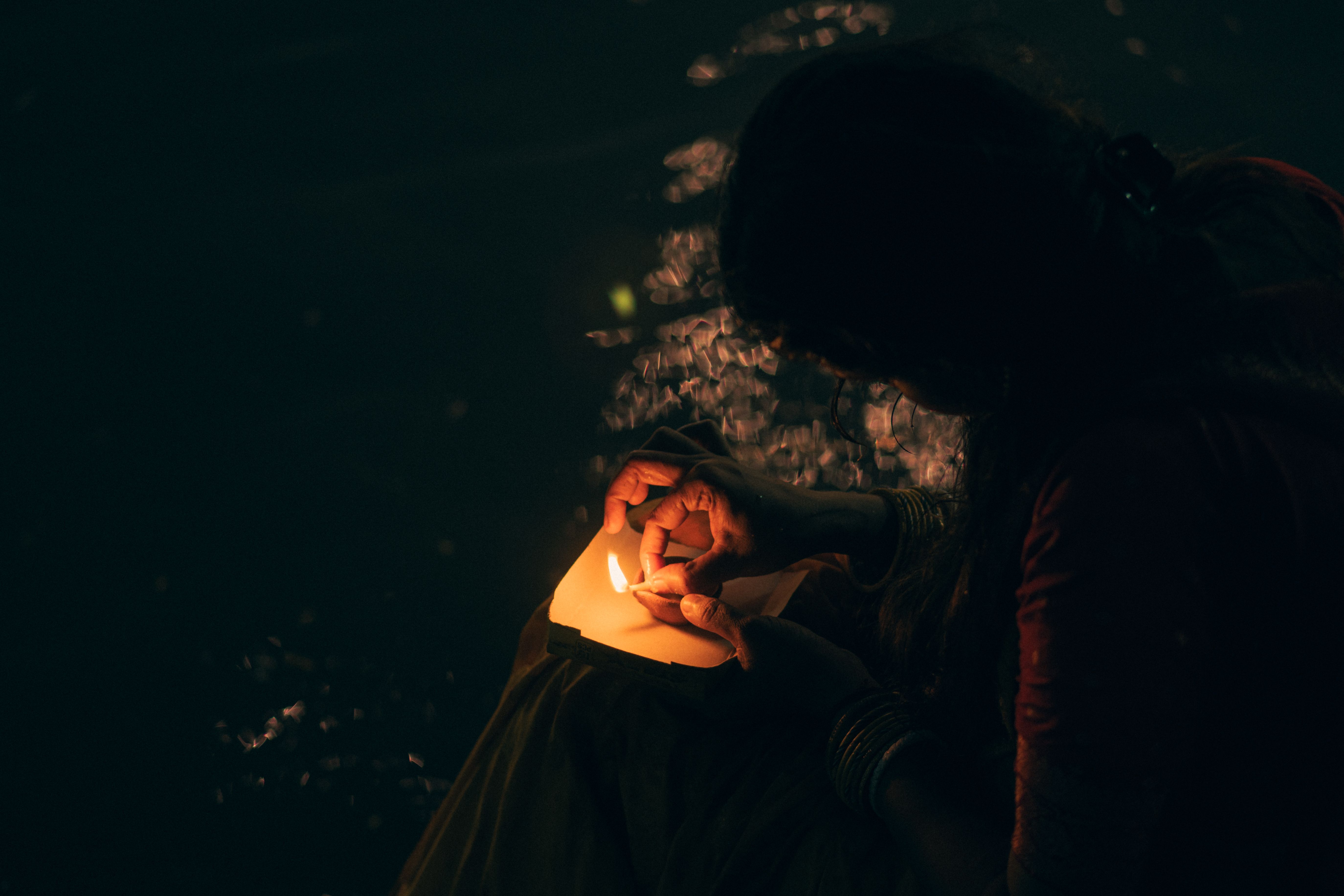 A woman lights a small diya in the dark, a quiet way to honor the ancestors during Pitru Paksha