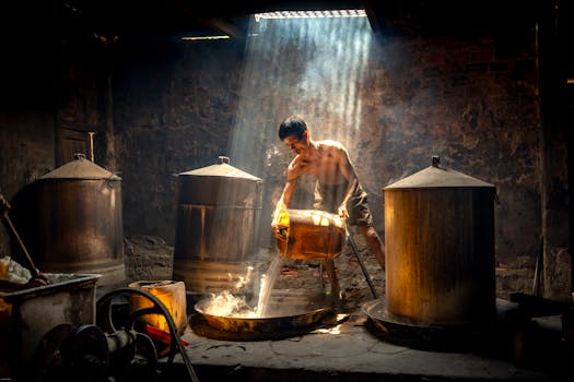 Man engaged in traditional brewing inside rustic environment, illuminated by natural light beams.