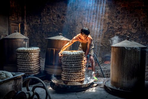 Free A man preparing rice cakes in an artisanal steam kitchen, illuminated by natural light. Stock Photo