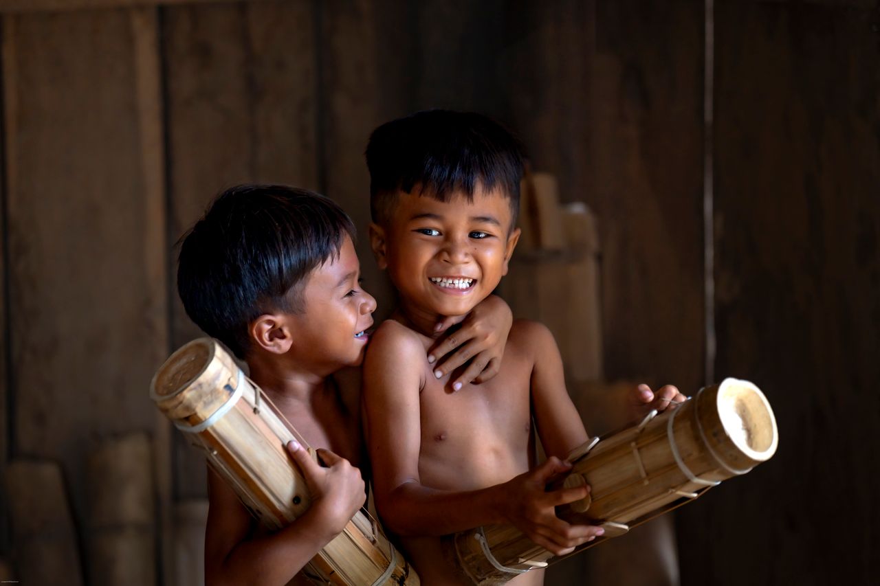 two smiling children playfully holding bamboo sticks in a dimly lit in