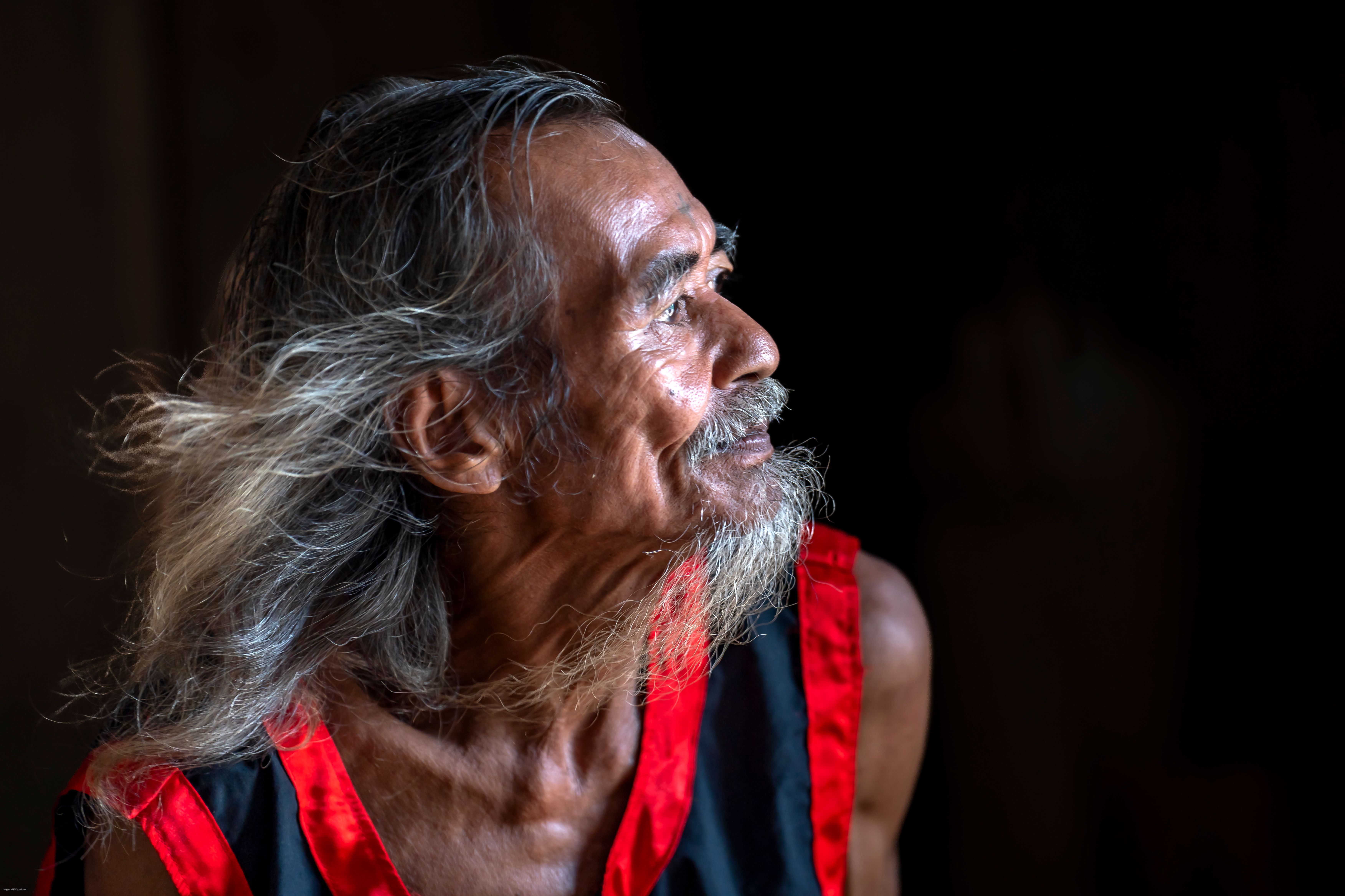 Portrait of an elderly man with long hair, wearing a traditional outfit, gazing thoughtfully.