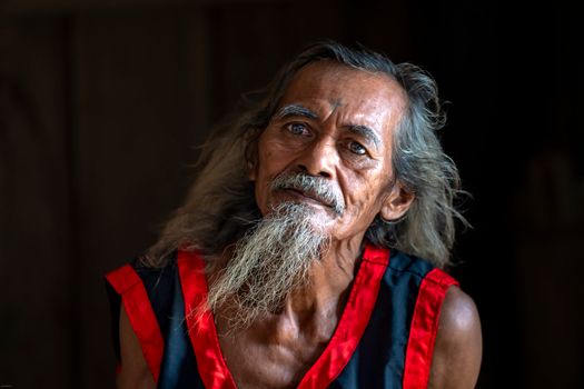 Thoughtful elderly man with long beard and traditional attire, captured indoors with dramatic lighting.