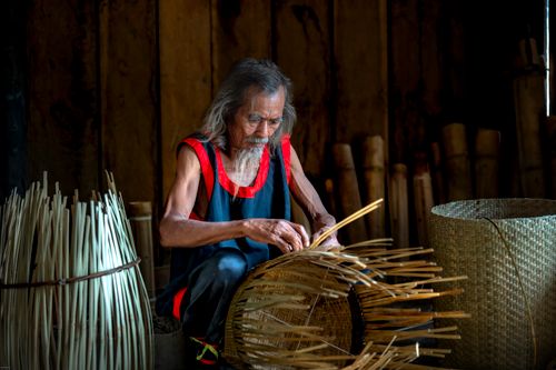 Free Elderly man crafting a bamboo basket indoors, showcasing traditional weaving skills. Stock Photo