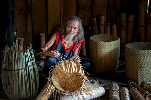 Free An elderly man skillfully weaving a basket in a rustic indoor setting, showcasing traditional craftsmanship. Stock Photo