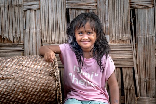 A joyful child sitting by a wicker basket in a rustic setting with a woven background.