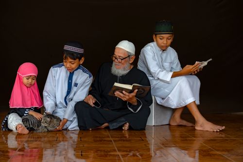 Free A family of four reading indoors with a cat, highlighting cultural and familial bonds. Stock Photo