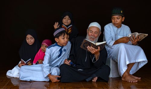 Free Diverse group of Muslims of all ages sharing a moment of reading the Quran together, fostering cultural and religious bonds. Stock Photo