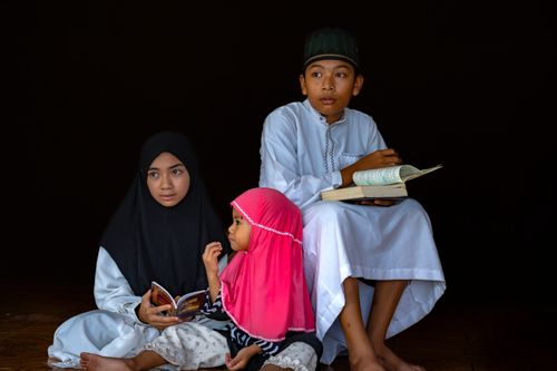 Free A group of three children in traditional attire reading religious texts with focus and concentration. Stock Photo