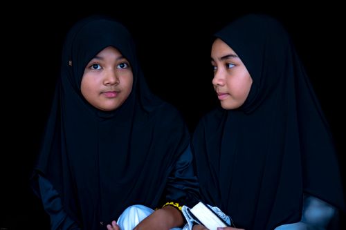 Free Close-up portrait of two girls wearing traditional hijabs with a dark background. Stock Photo
