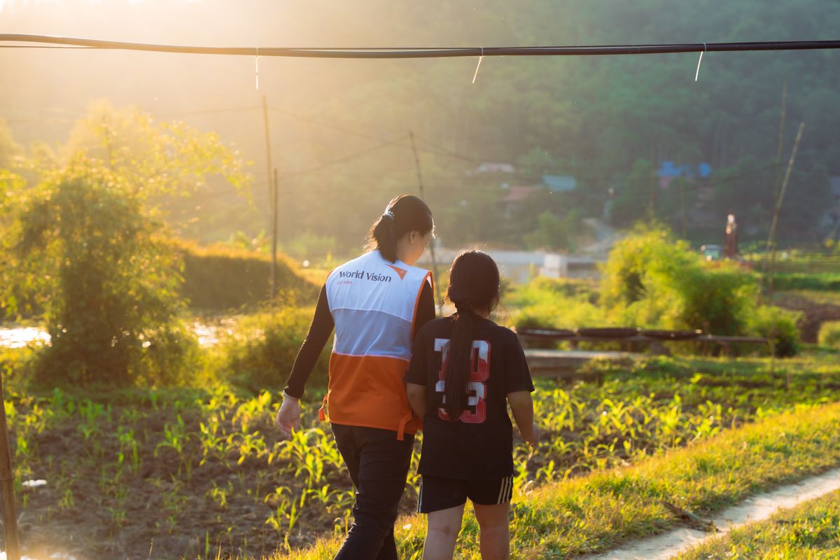 Field volunteer walking with a child at sunset in a rural area