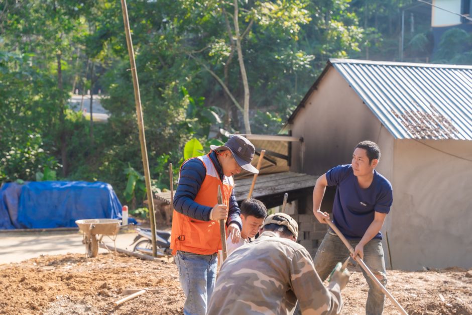 A diverse team of workers collaborates on an outdoor construction site surrounded by greenery.