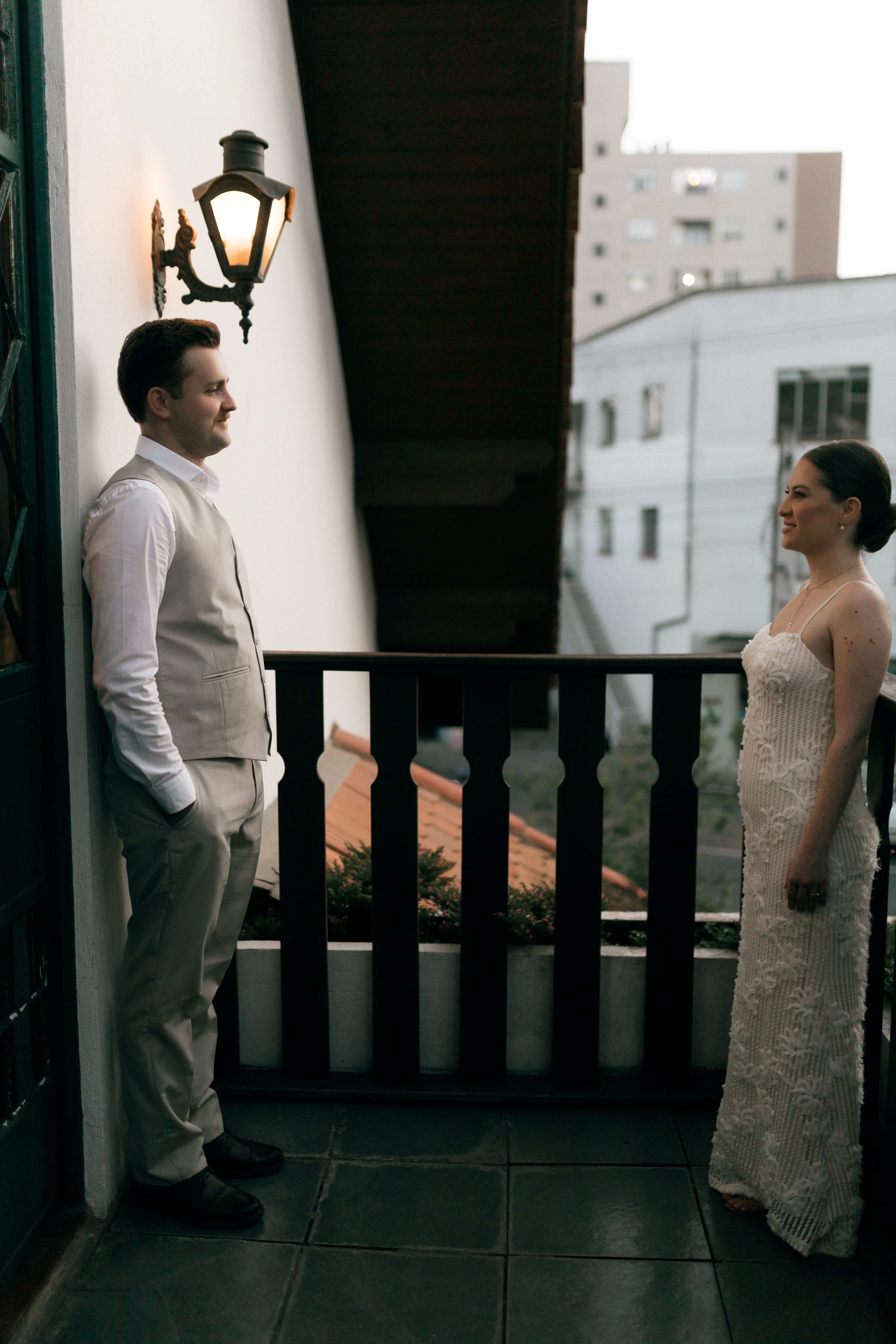 A couple dressed elegantly sharing a private moment on a balcony with a city view.
